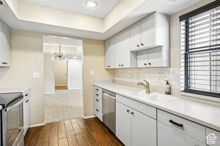 White cabinetry with black hardware, white countertops, stainless steel appliances, tile backsplash, and wood-finish flooring
