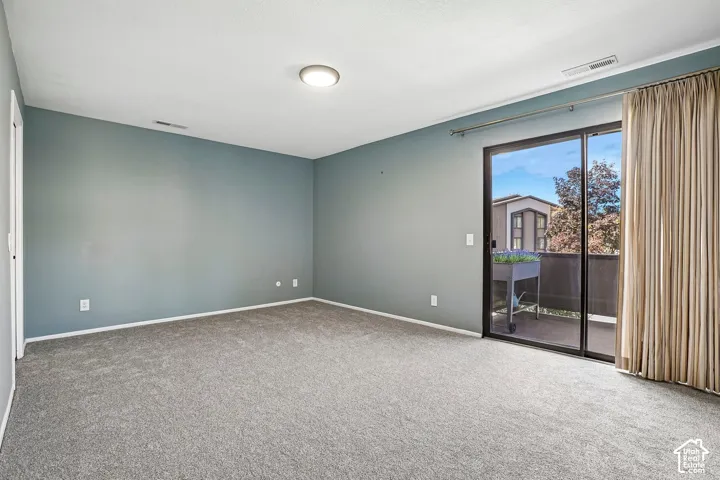 Spacious room with gray carpeting, blue walls, a ceiling-mounted light fixture, and a sliding glass door leading to a private outdoor balcony