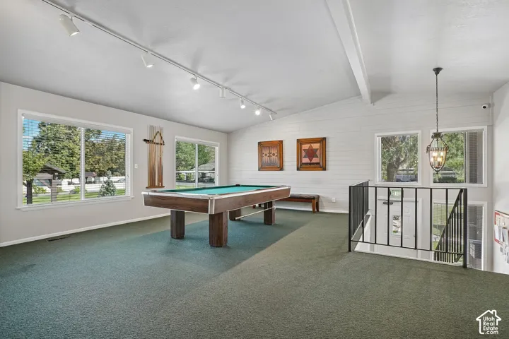 Vaulted ceiling with exposed beams, track lighting, multiple windows, and a built-in railing