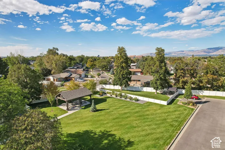Expansive green space featuring a covered pavilion, mature trees, landscaped planting beds, and a paved pathway
