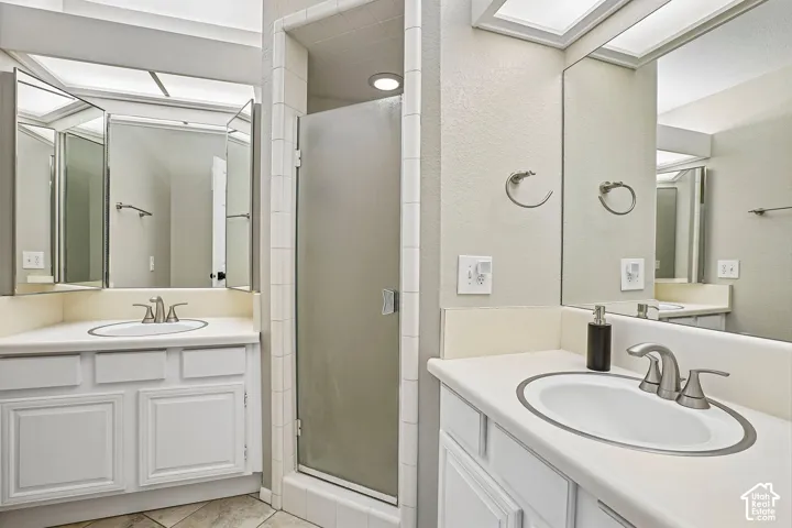 Dual-sink bathroom featuring white cabinetry with multiple storage drawers, ceramic countertops, and chrome faucet fixtures