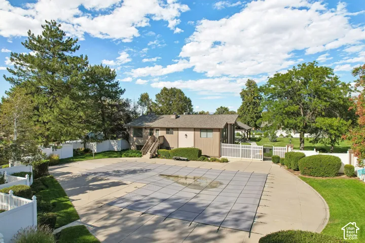 Fenced-in outdoor pool with a cover, concrete decking, and surrounding green landscaping