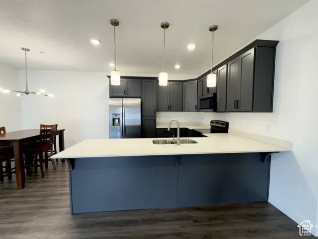 Modern kitchen featuring dark cabinetry, stainless steel appliances, a quartz center island with pendant lighting, and wood-finish flooring