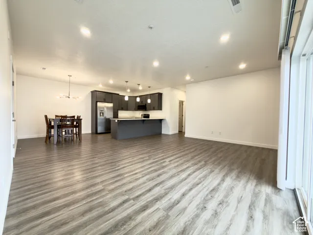 Spacious open-concept layout with wood-finish flooring, recessed lighting, and a contemporary kitchen featuring dark cabinetry, an island, and stainless steel appliances