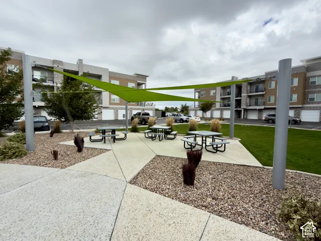 Outdoor common area featuring a shade sail, multiple picnic tables, concrete patio, and gravel landscaping
