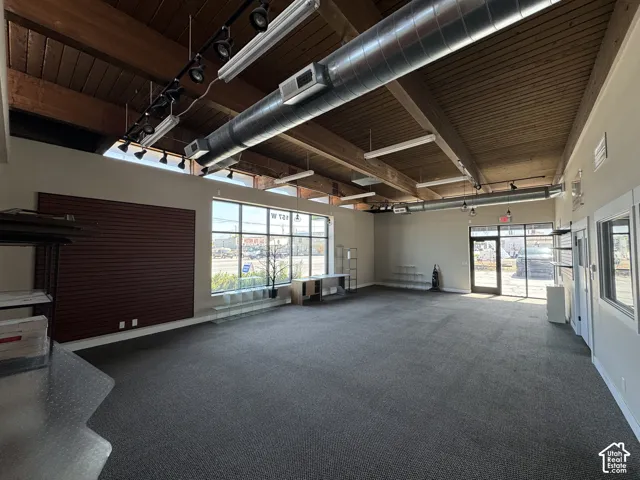 Expansive commercial space featuring high ceilings with exposed wood beams, track lighting, and abundant natural light from large storefront windows