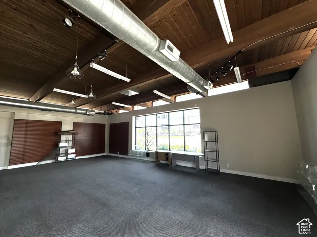 Exposed wood beam ceiling, industrial-style pendant lighting, track lighting, full-height window, and gray carpet flooring