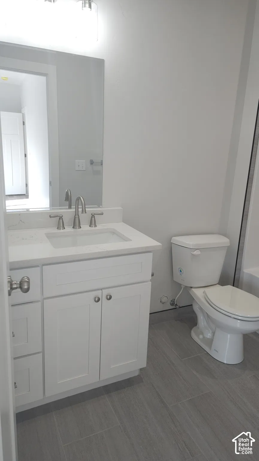 White vanity with an integrated sink and brushed nickel hardware, set against gray plank-style floor tiling