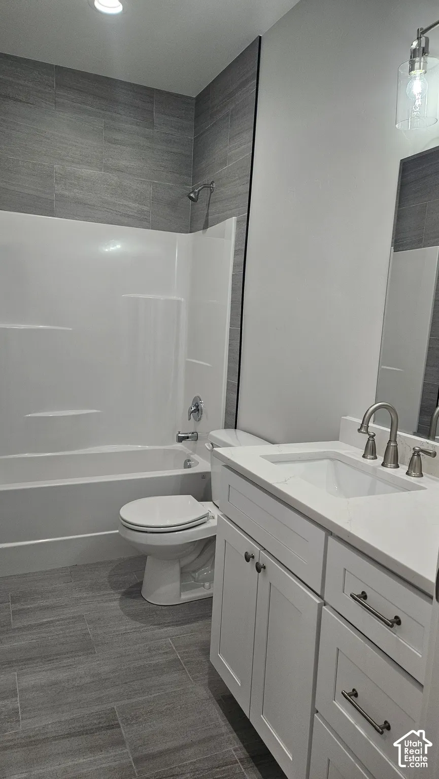 Bathroom featuring a white vanity with integrated sink, brushed nickel faucet, tiled shower surround, and gray wood-finish flooring