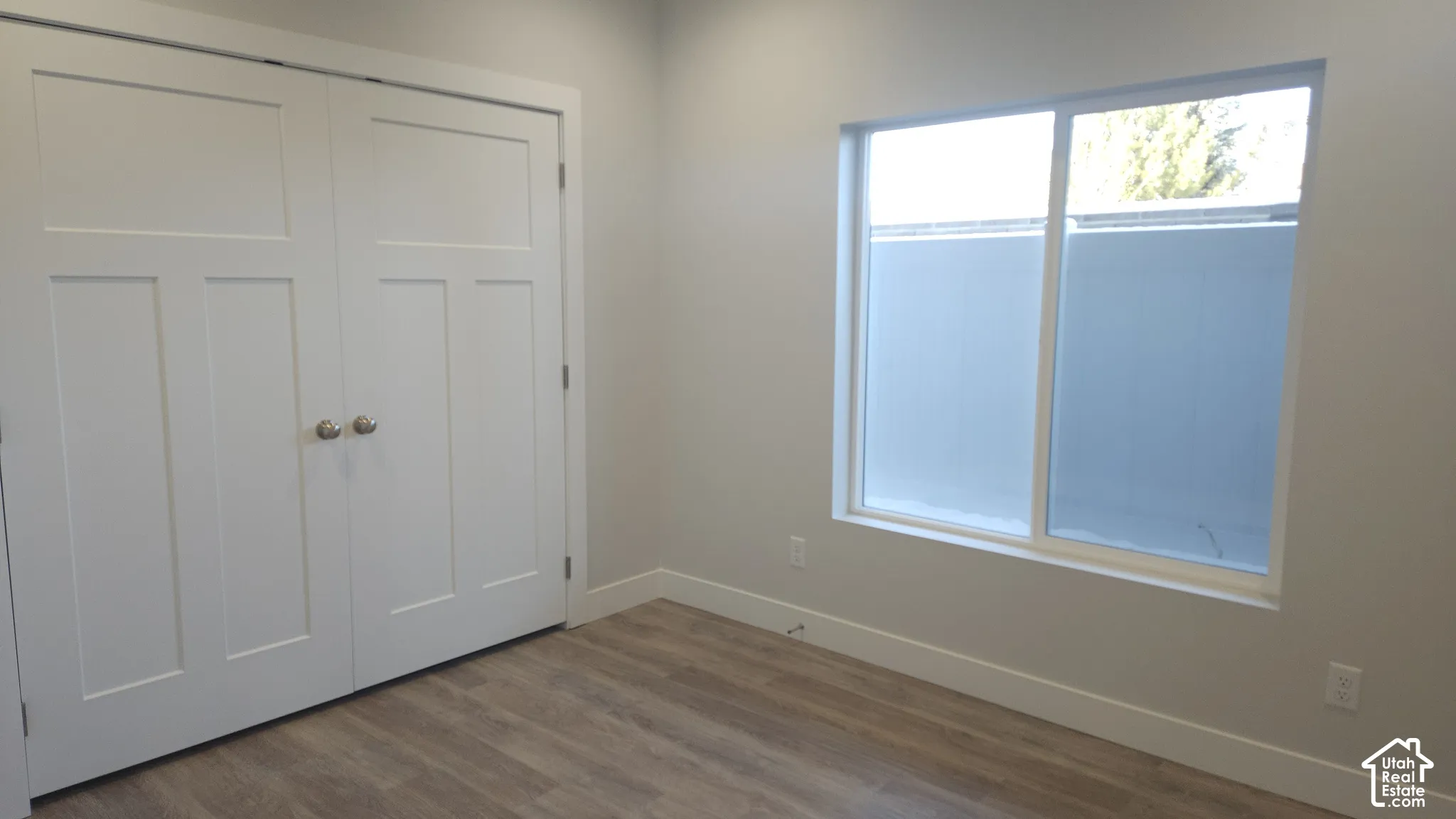Wood-finish flooring, white trim, white paneled bifold doors, and a large window with privacy film