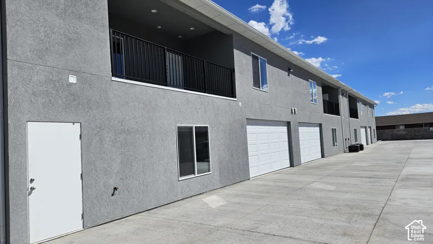 Stucco exterior with multiple garage bays, individual entry doors, upper-level balconies with black railings, and multiple windows