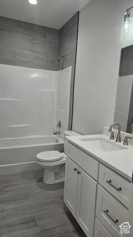Bathroom featuring a white vanity with integrated sink, brushed nickel faucet, tiled shower surround, and gray wood-finish flooring