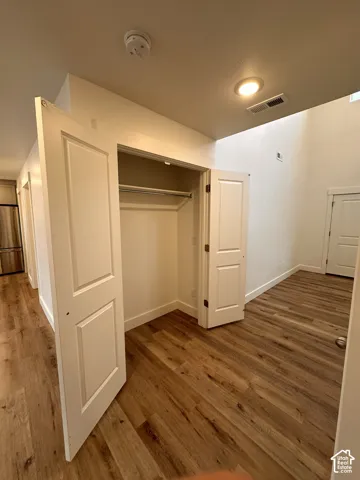 Wood-finish flooring throughout, featuring a recessed ceiling light, white paneled doors, and a built-in closet with a hanging rod and shelf