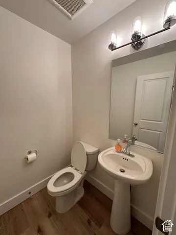 Pedestal sink with chrome faucet, wall-mounted mirror, modern vanity lighting, wood-finish flooring, and white wall paint