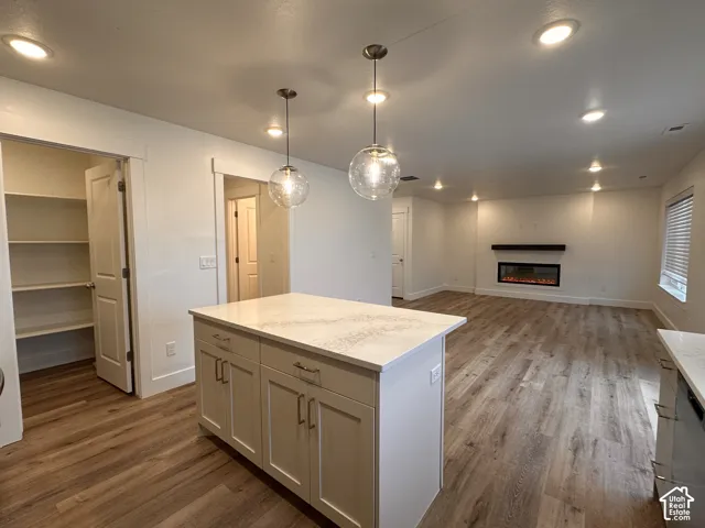 Kitchen island with light-toned cabinetry and a light-toned countertop, wood-finish flooring, recessed lighting, and an electric fireplace with a dark mantel