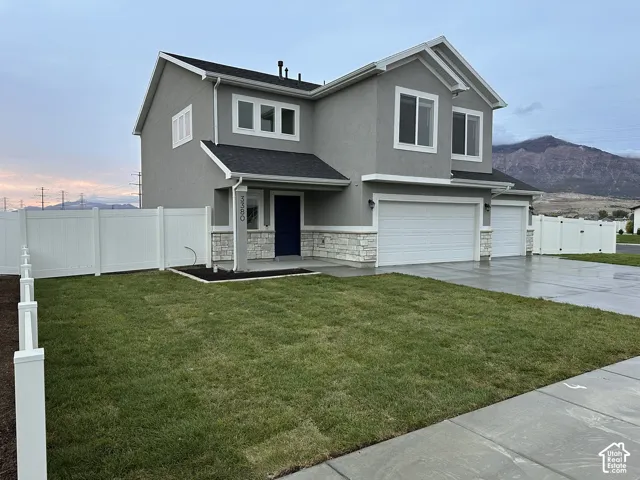 Contemporary stucco exterior with stone accents, two-car garage, dark asphalt shingle roof, and a white privacy fence