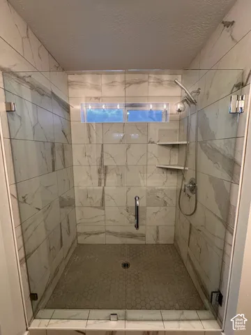 Glass-enclosed shower with large format wall tiles, hexagonal floor tiles, built-in shelving, and a window
