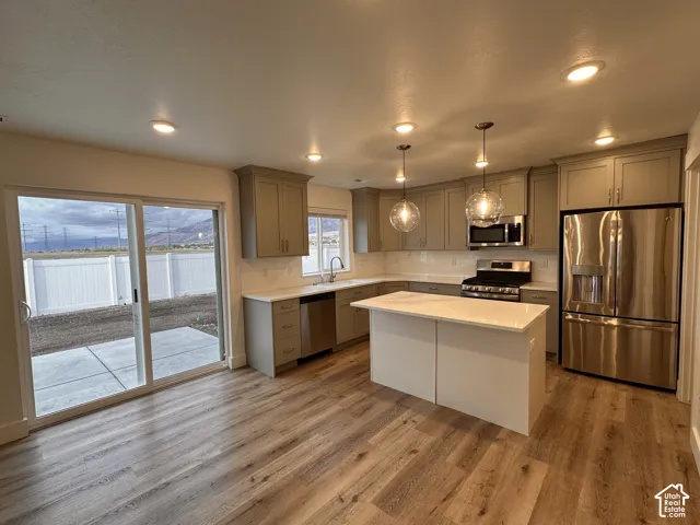 Kitchen featuring wood-finish flooring, recessed lighting, pendant lighting, stainless steel appliances, and a central island with a solid surface countertop