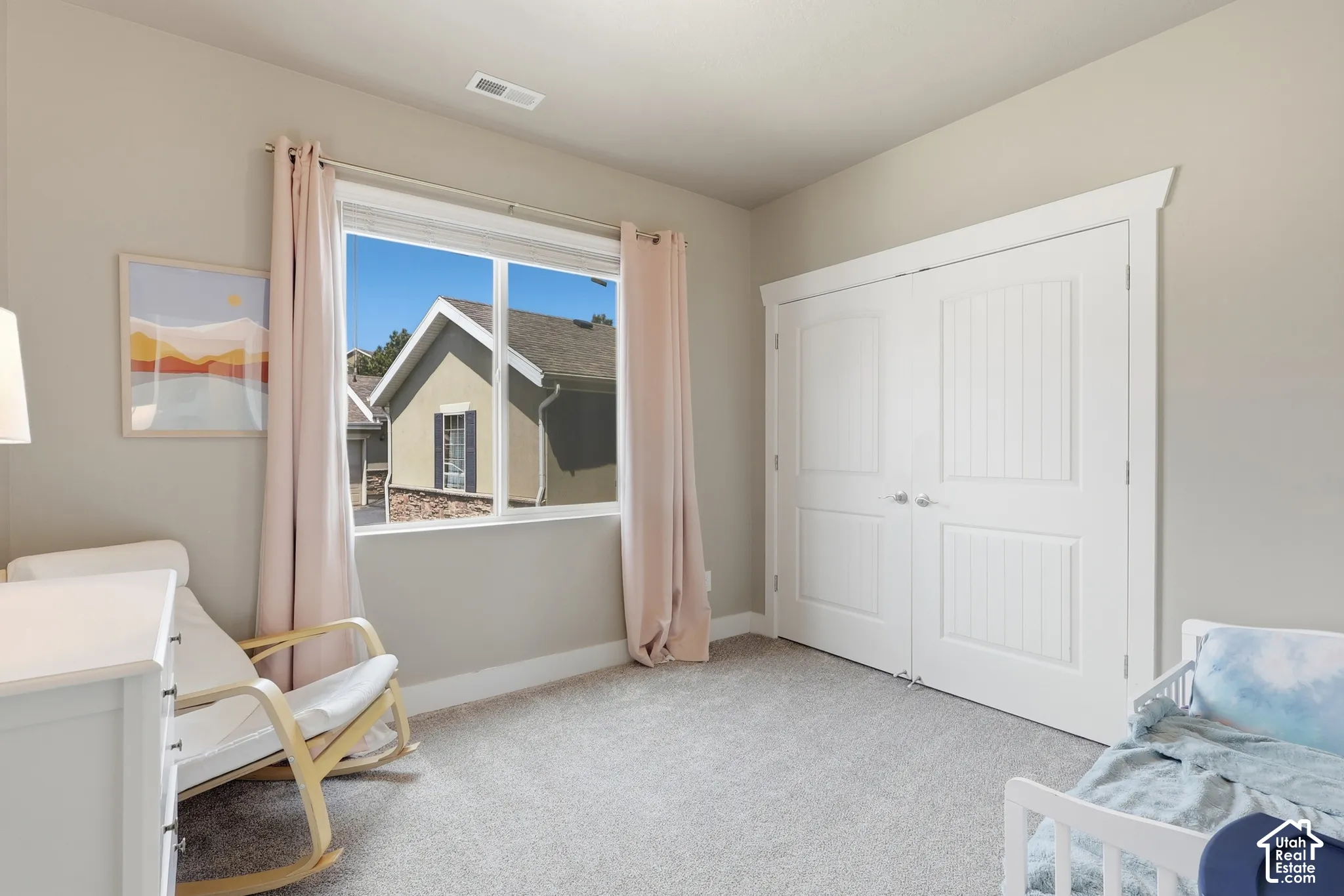 Neutral-toned room featuring a large window with white trim, light-colored carpeting, a double-door closet with vertical paneling, and baseboard molding