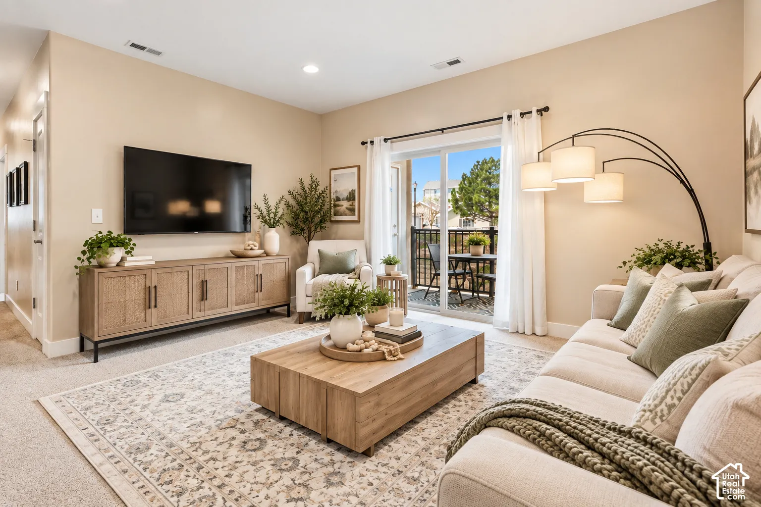 Sliding glass door leading to a private outdoor balcony, recessed ceiling lighting, wall-mounted television, and a wood-finish media console