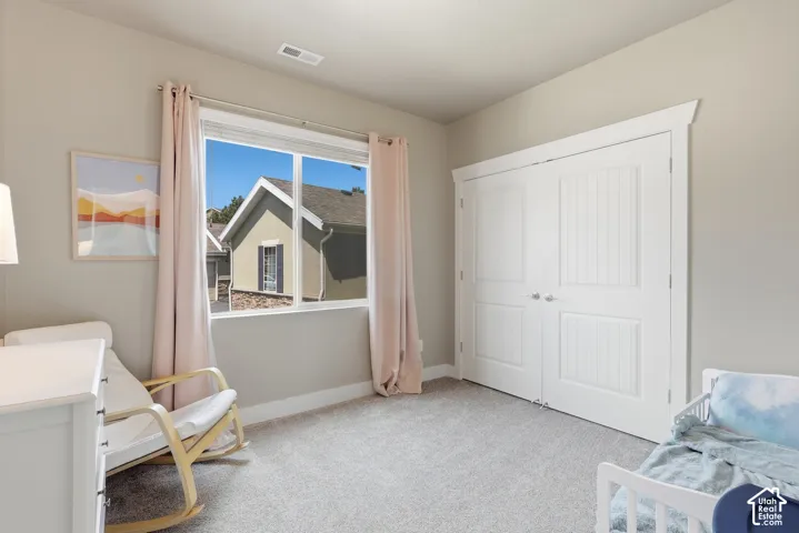Neutral-toned room featuring a large window with white trim, light-colored carpeting, a double-door closet with vertical paneling, and baseboard molding