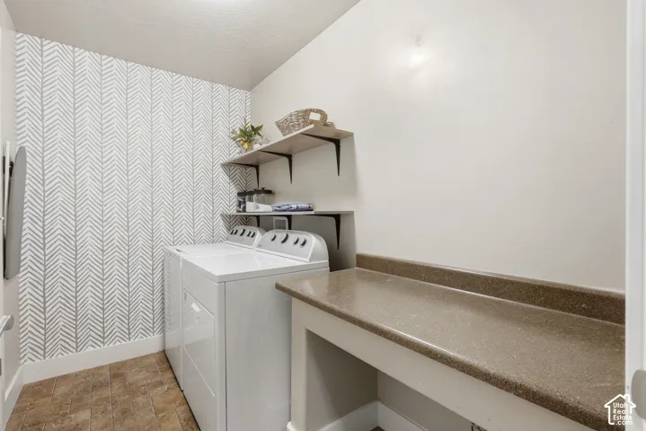 Laundry room featuring patterned accent wall, tile flooring, built-in countertop, and two wall-mounted shelves