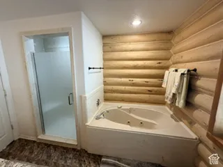 Jetted soaking tub, glass-enclosed shower, log-style wall paneling, recessed lighting, and tile flooring