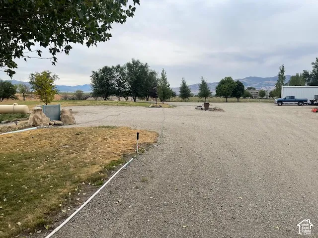 Expansive gravel lot with mature trees, mountain range backdrop, and propane tank
