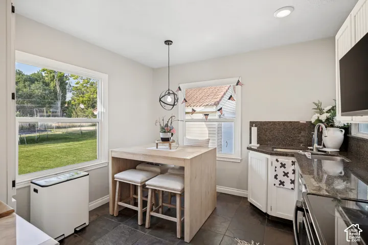 Kitchenette featuring stone tile flooring, a built-in counter-height table, a pendant light fixture, a corner sink with stone countertops, and white cabinetry