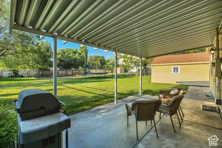Covered patio with a concrete surface, expansive lawn, and a detached shed featuring a tile roof and siding