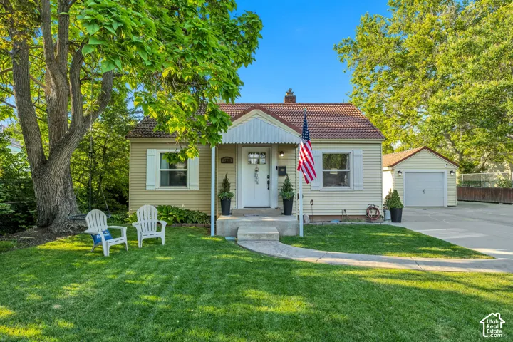 Well-manicured front lawn, mature shade tree, concrete walkway, detached garage, and concrete driveway