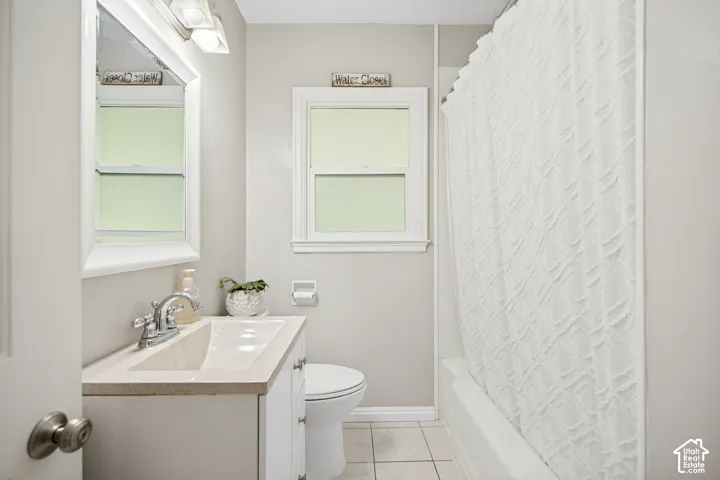 Vanity with integrated sink, window with trim, tile flooring, and a shower/tub combination