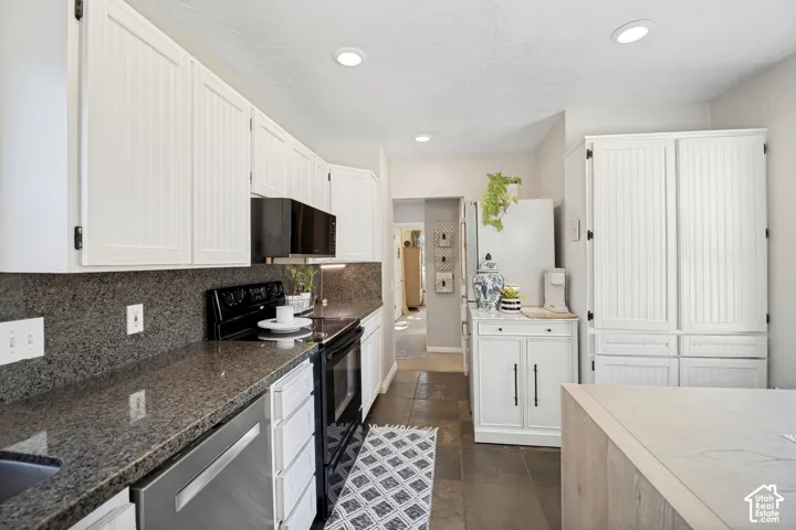 White paneled cabinetry, dark stone countertops, stainless steel dishwasher, black range, and recessed lighting
