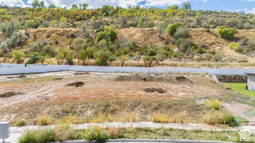 Expansive lot featuring a level building area, a white perimeter fence, and a backdrop of natural hillside landscaping