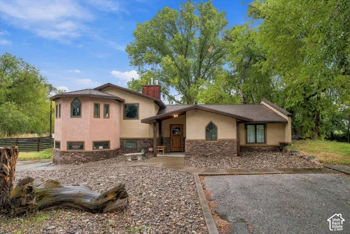 Stucco exterior with stone accenting, prominent round tower element, gabled entry porch, asphalt shingle roofing, and a stone chimney