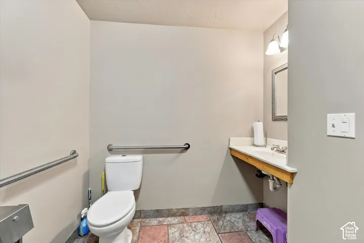 Powder room featuring a white toilet, wall-mounted grab bars, corner vanity with an integrated sink, framed mirror, and mosaic tile flooring