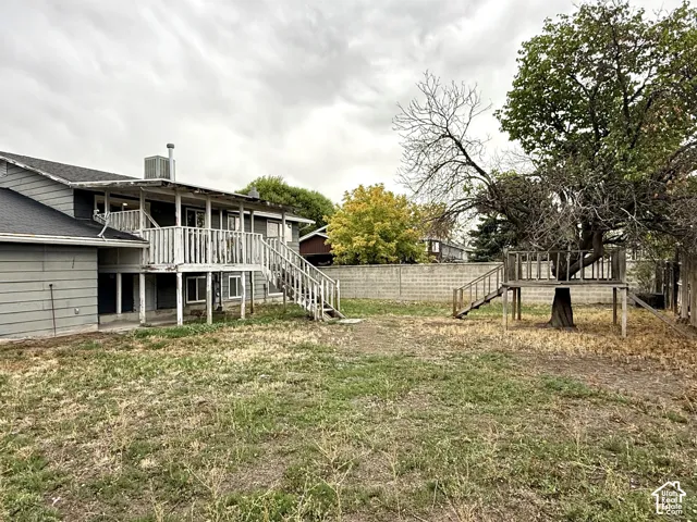 Expansive backyard featuring a multi-level deck with stairs, a built-in play structure, a concrete block fence, and mature trees