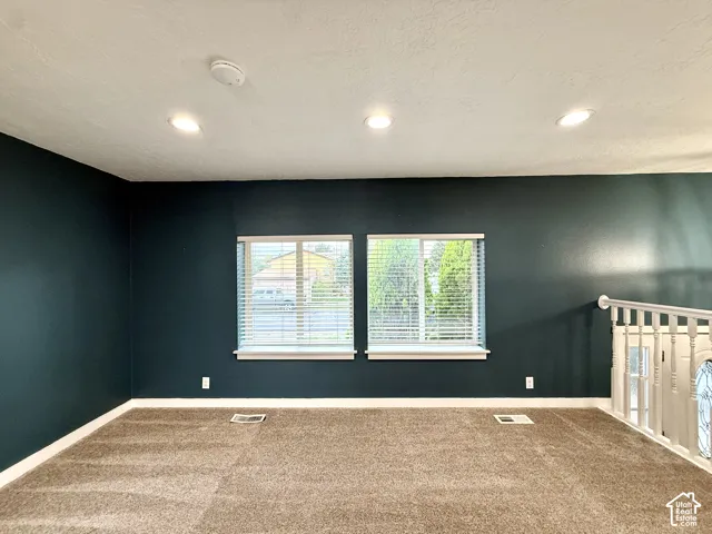 Dark-toned accent wall, recessed ceiling lighting, two windows with horizontal blinds, carpeting, and white painted railing