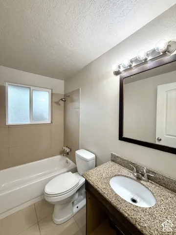 Bathtub with tiled surround, single vanity with light-toned countertop, and framed mirror