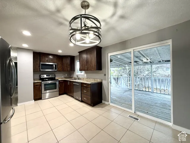 Kitchen featuring dark wood cabinetry, stainless steel appliances, light-toned tile flooring, recessed lighting, and a contemporary chandelier