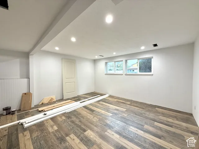 Recessed lighting, wood-finish flooring, white paneled walls, three windows, and a paneled door