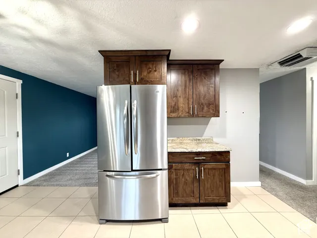 Tile flooring, stainless steel refrigerator, wood-finish cabinetry, light-toned countertop, recessed lighting
