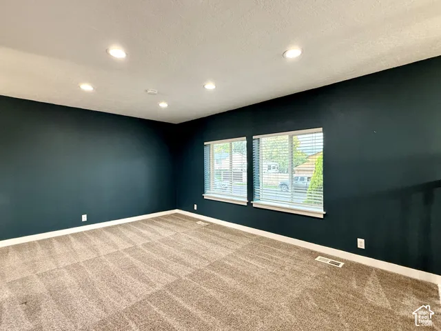 Recessed lighting, dark accent wall, two windows with blinds, and neutral-toned carpeting