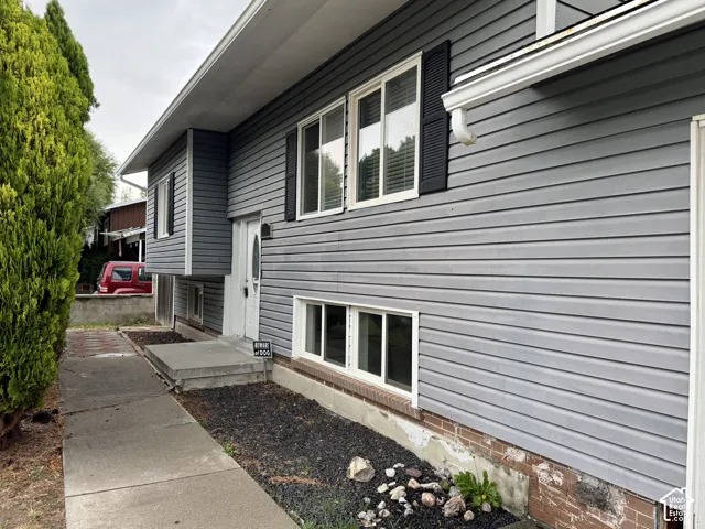 Gray horizontal siding exterior with a white entry door, multiple windows, and a concrete pathway