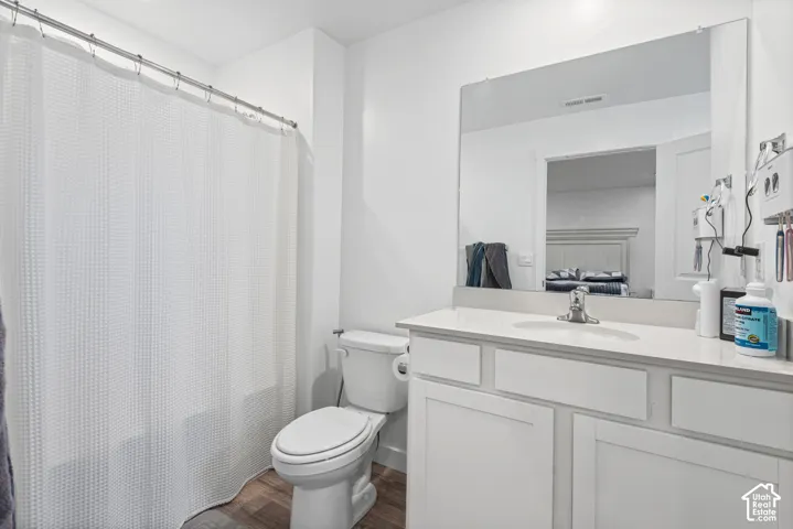 Wood-finish flooring with a white vanity featuring a single basin sink, white countertop, and framed mirror