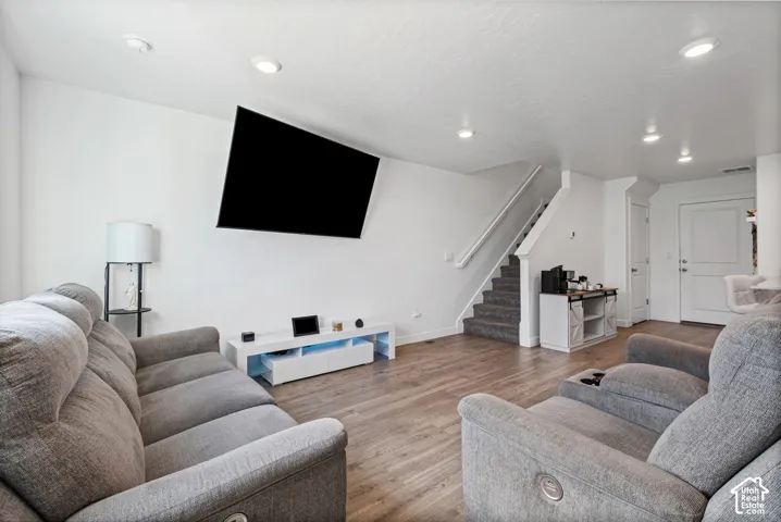 Recessed ceiling lighting, wood-finish flooring, white walls, and a carpeted staircase with white railings