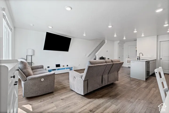 Open-concept living space featuring wood-finish flooring, recessed lighting, white walls, and a kitchen island with a sink and a stainless steel faucet