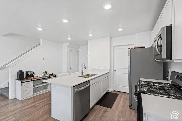 Kitchen featuring white cabinetry, stainless steel appliances, a center island with sink, white countertops, and wood-finish flooring