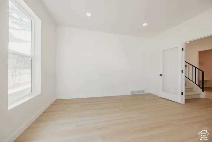 Recessed lighting, wood-finish flooring, large window, frosted glass door, and staircase with black metal railing