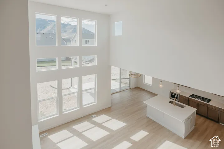Two-story living area with abundant natural light, a contemporary kitchen island featuring a sink and faucet, integrated kitchen appliances including a cooktop and microwave, and wood-finish flooring throughout